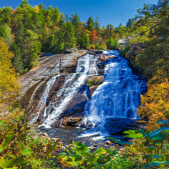 Waterfall cascading over rocky ledges surrounded by colorful autumn trees in a forest landscape