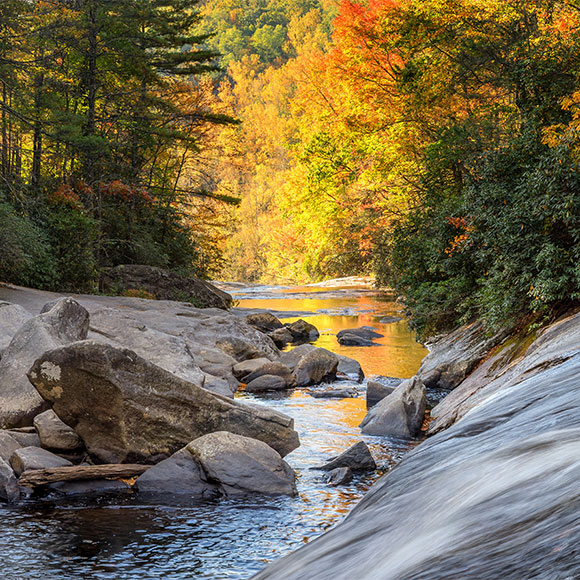 Autumn forest river with colorful orange and yellow foliage and large rocks along a shallow stream runoff meltwater flowing over a rock ledge