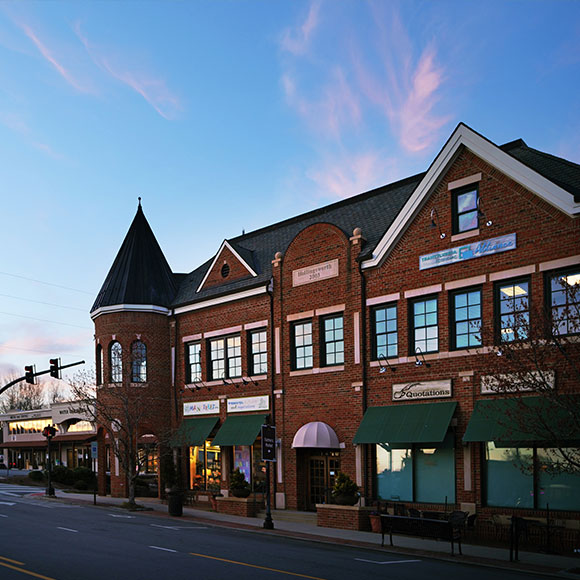 Brick storefront building on a quiet street with green awnings and a turret, blue sky at dusk.